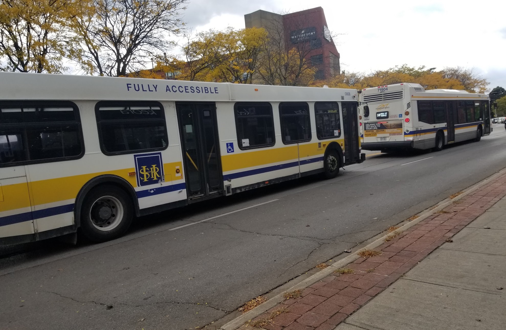 Two Burlington Transit buses driving one in front of the other along the road in downtown Burlington.