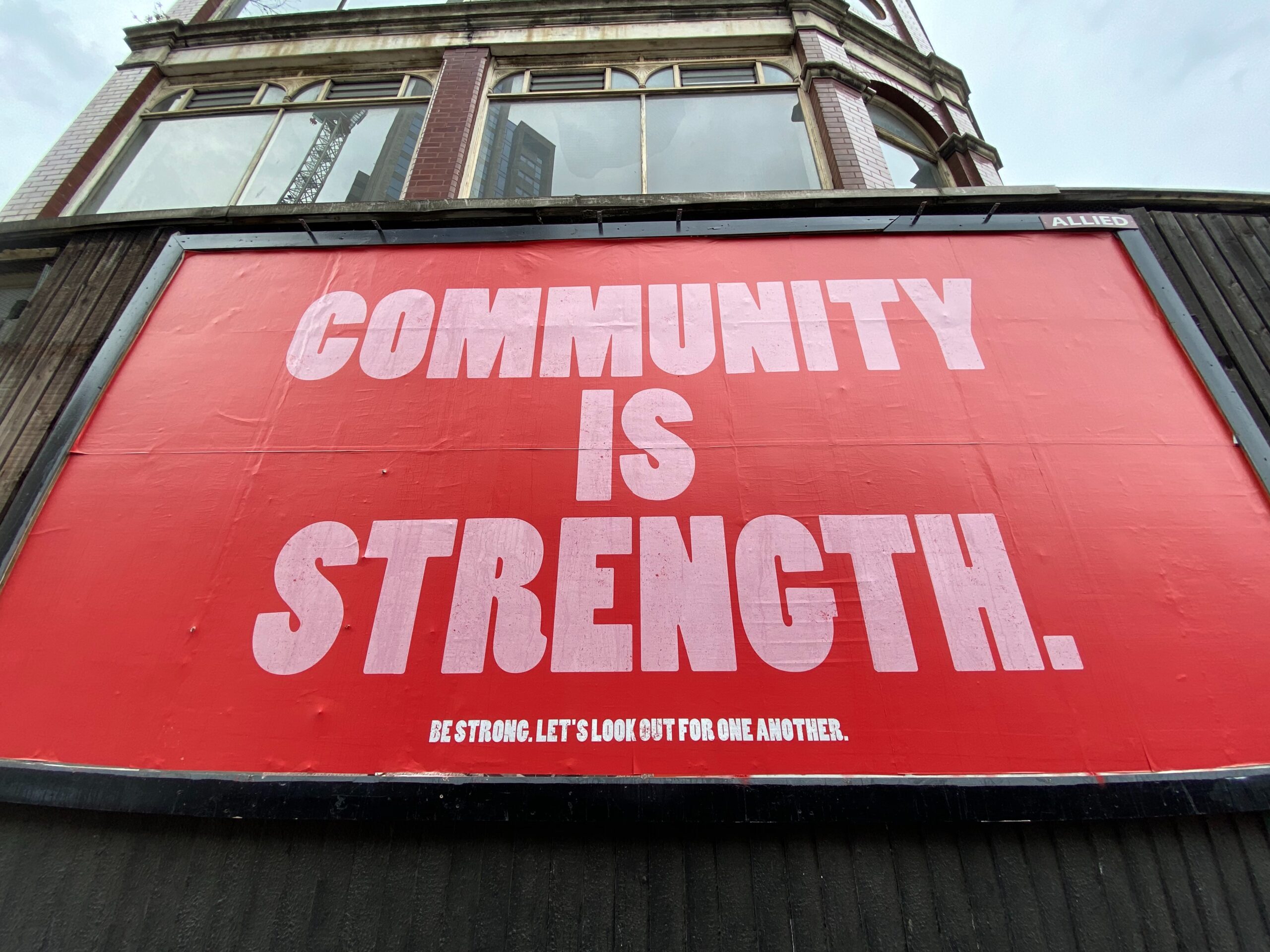 A large red sign on a wall, with two windows of a building visible behind it. The sign says "Community is Strength."