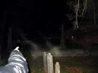 A cemetery at night, with an arm pointing at mists rising from the ground.