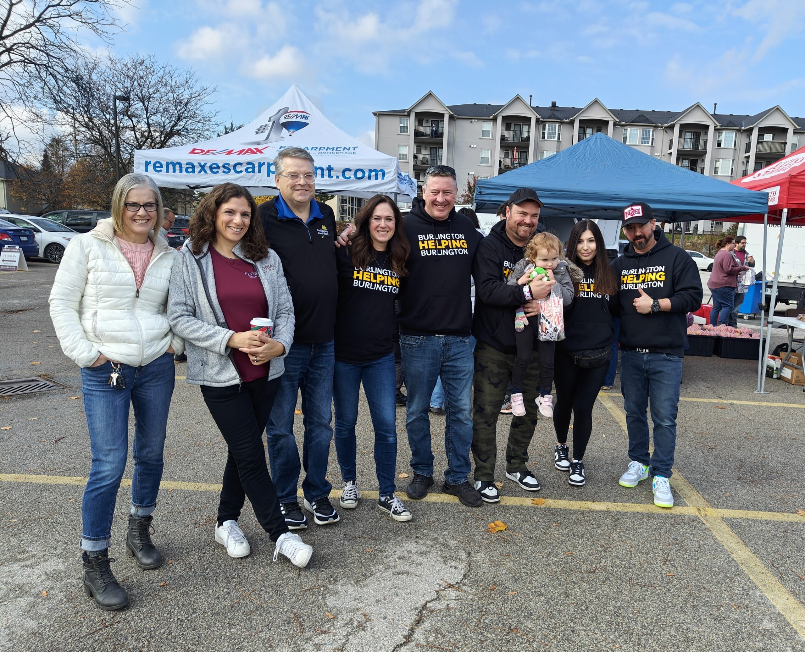 A group of nine people pose in a line at a Burlington Helping Burlington and Florian Realty food drive event.